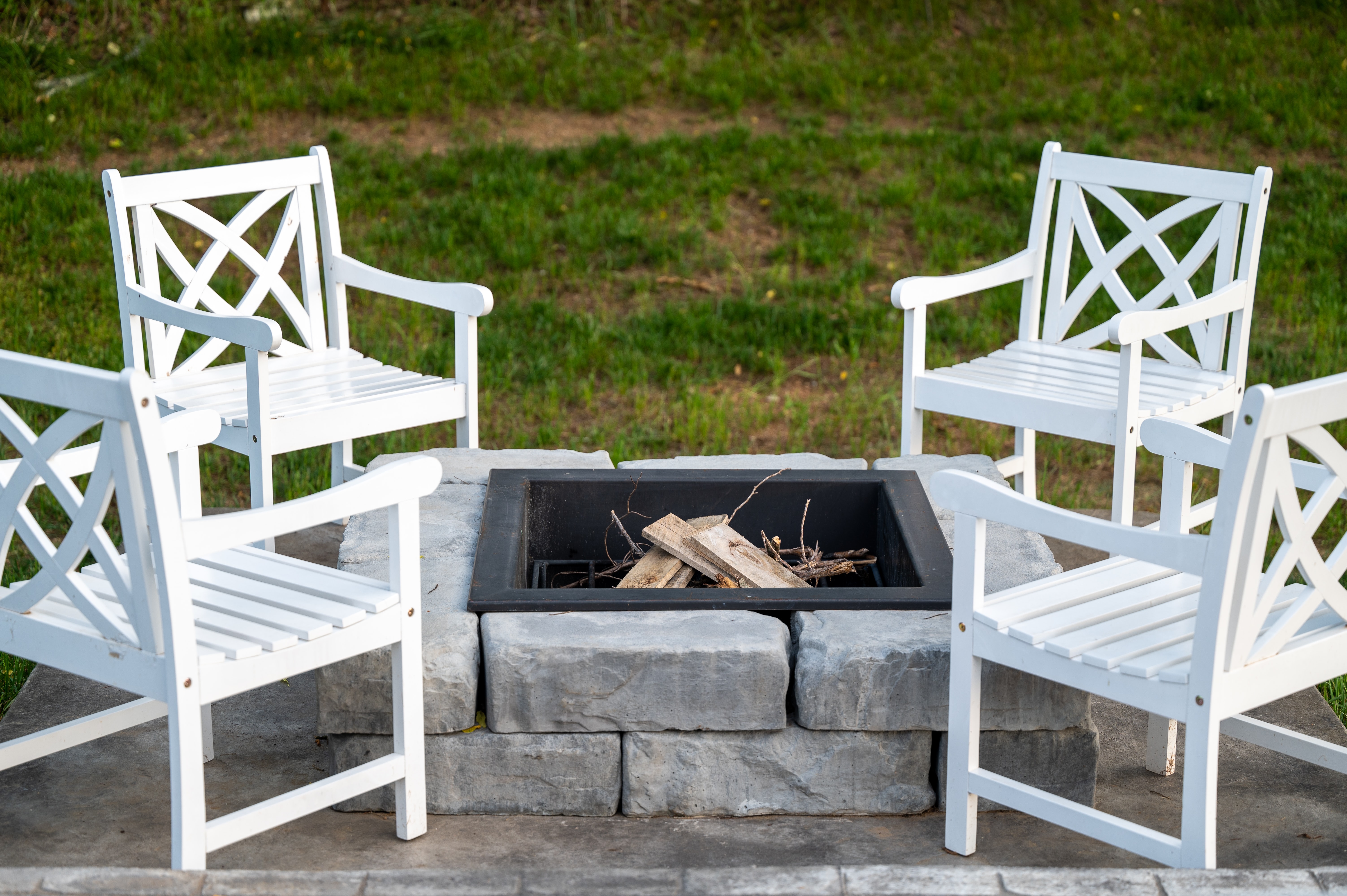 four white chairs surrounding outdoor stone fire pit