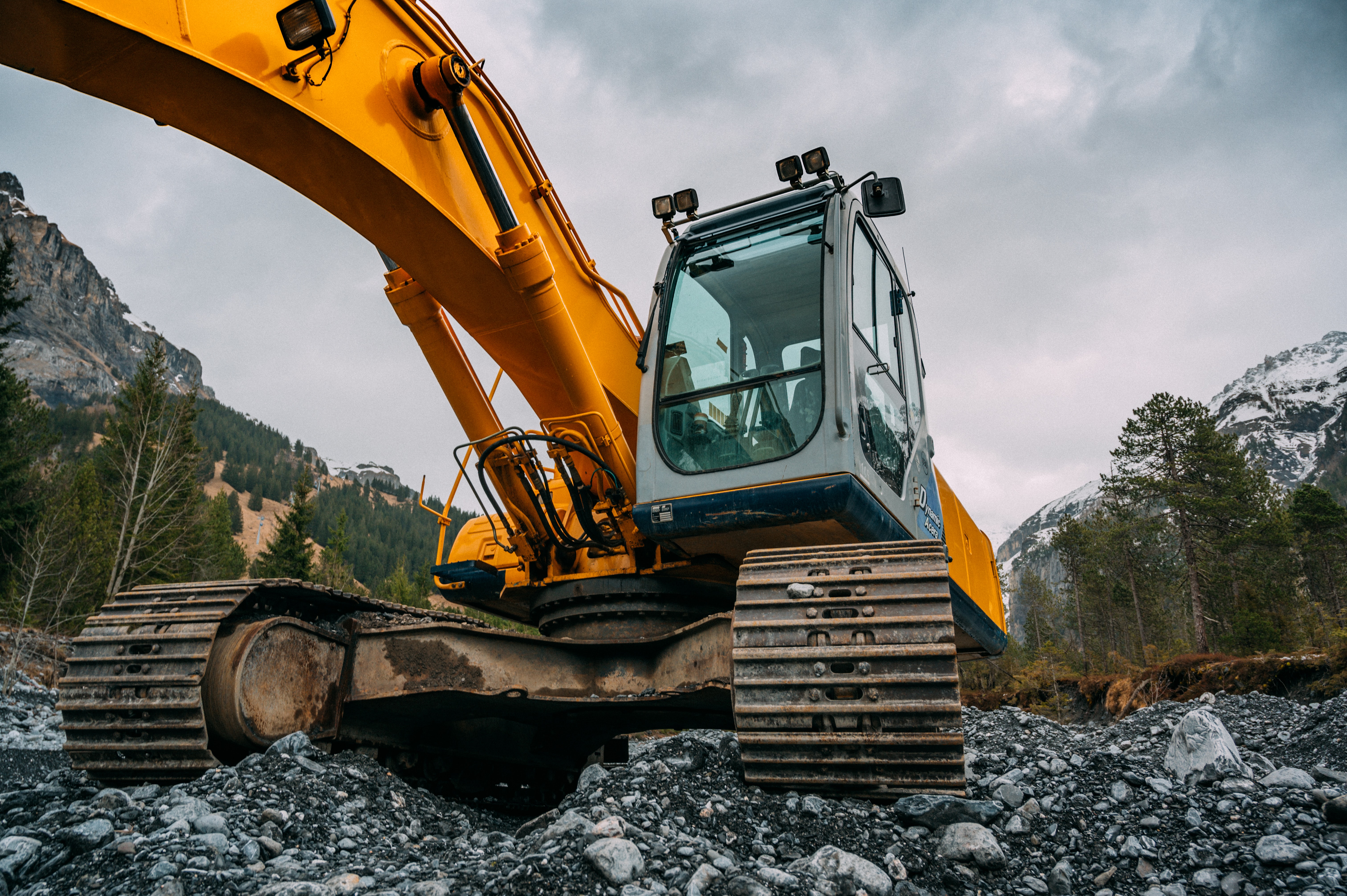 Yellow excavator in front of a forested mountain scene